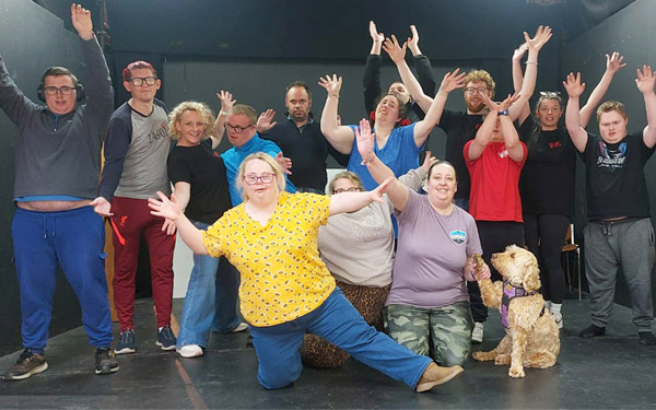 Group of people in bright colours and arms outstetched, with a honey coloured dog