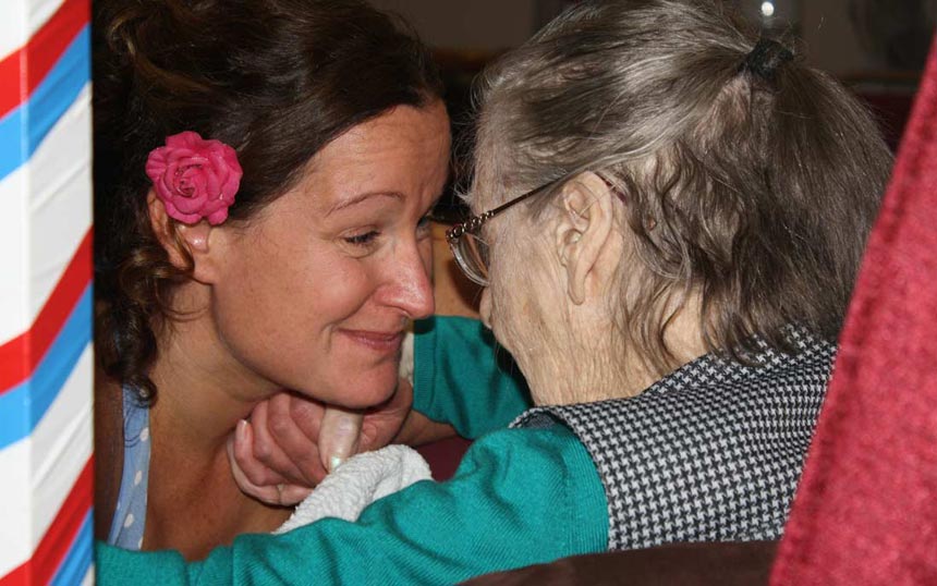 Woman with dark hair and red flower having eye contact with older woman with glasses